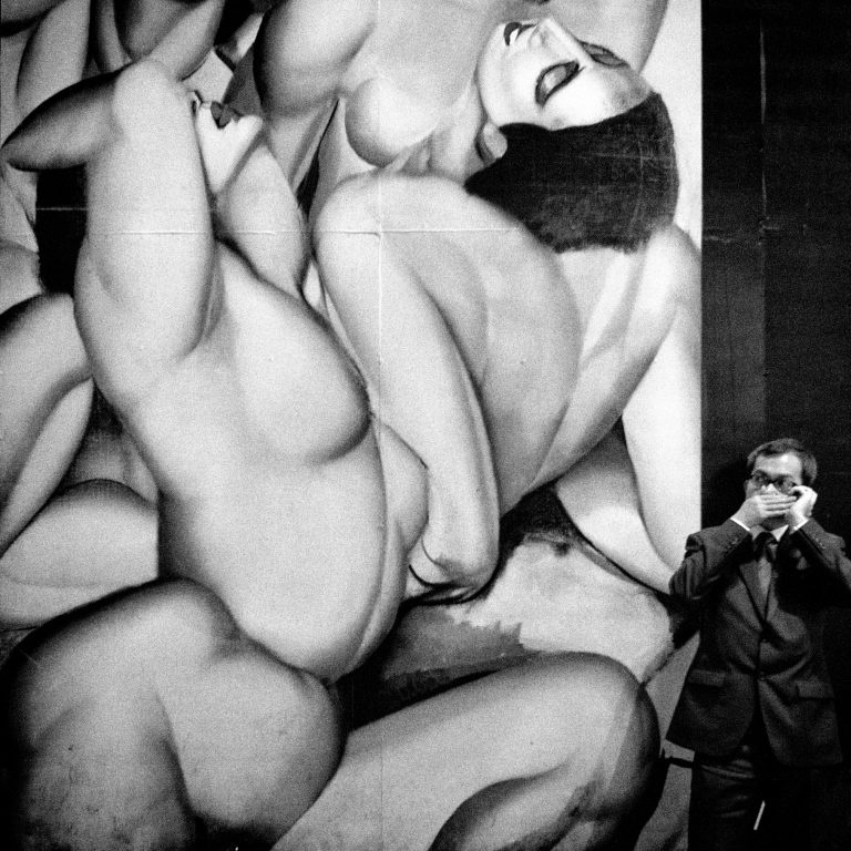 man on his cell phone standing in front of sign filled with bodies